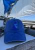 A blue Summer Sailstice hat on the cabin top of a sailboat with full jib out and blue skies beyond