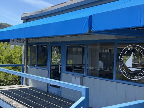 Image of the Modern Sailing office building with blue awning and the Modern Sailing logo on the windows at Clipper Yacht Harbor